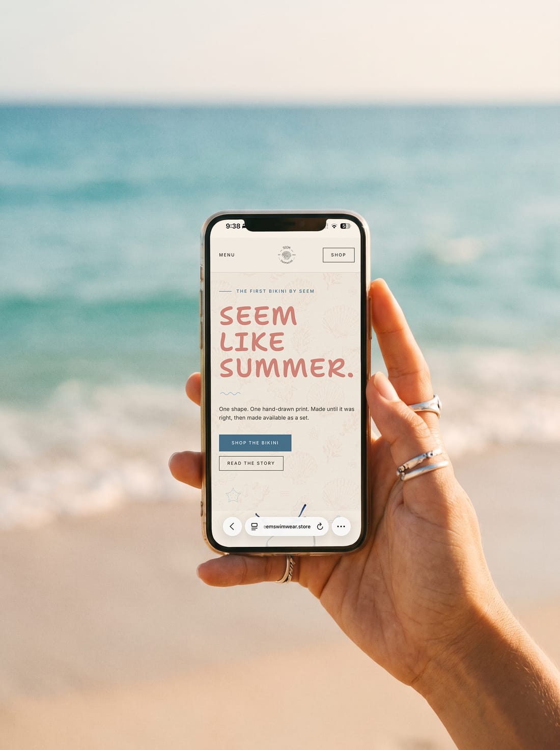 the seem swimwear homepage on a phone held up against the sea
